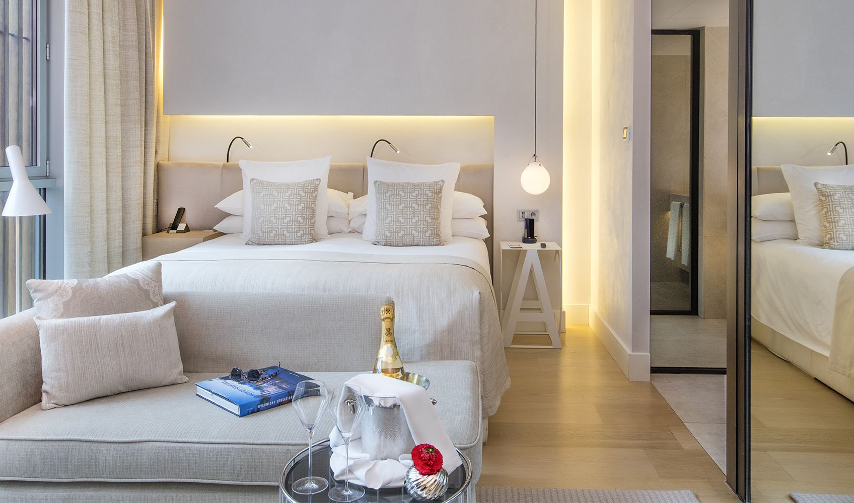 Een moderne hotelkamer met een groot bed, een bank en een kleintje tafeltje met een fles en glazen.