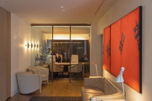 A modern interior with a glass partition, a desk with two chairs, a sofa, and a large orange artwork. - ABaC Hotel Boutique 5 GL (Barcelona)