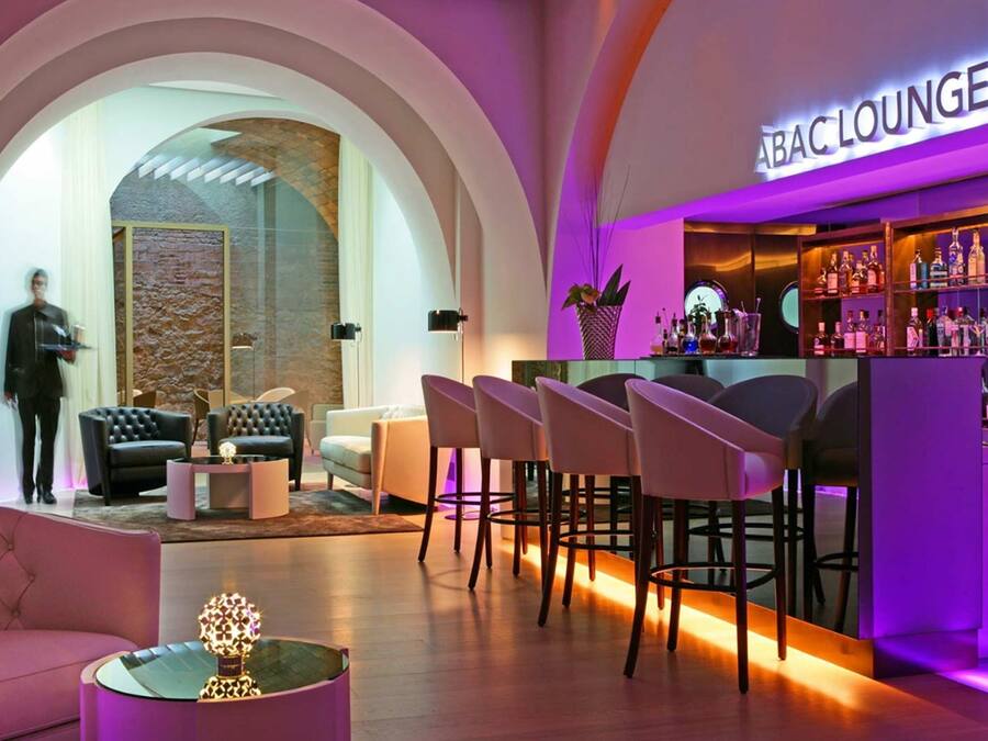 Un área de bar o lounge con diseño moderno, que incluye una barra con una variedad de botellas y una zona de estar con sillones y sofás de cuero.