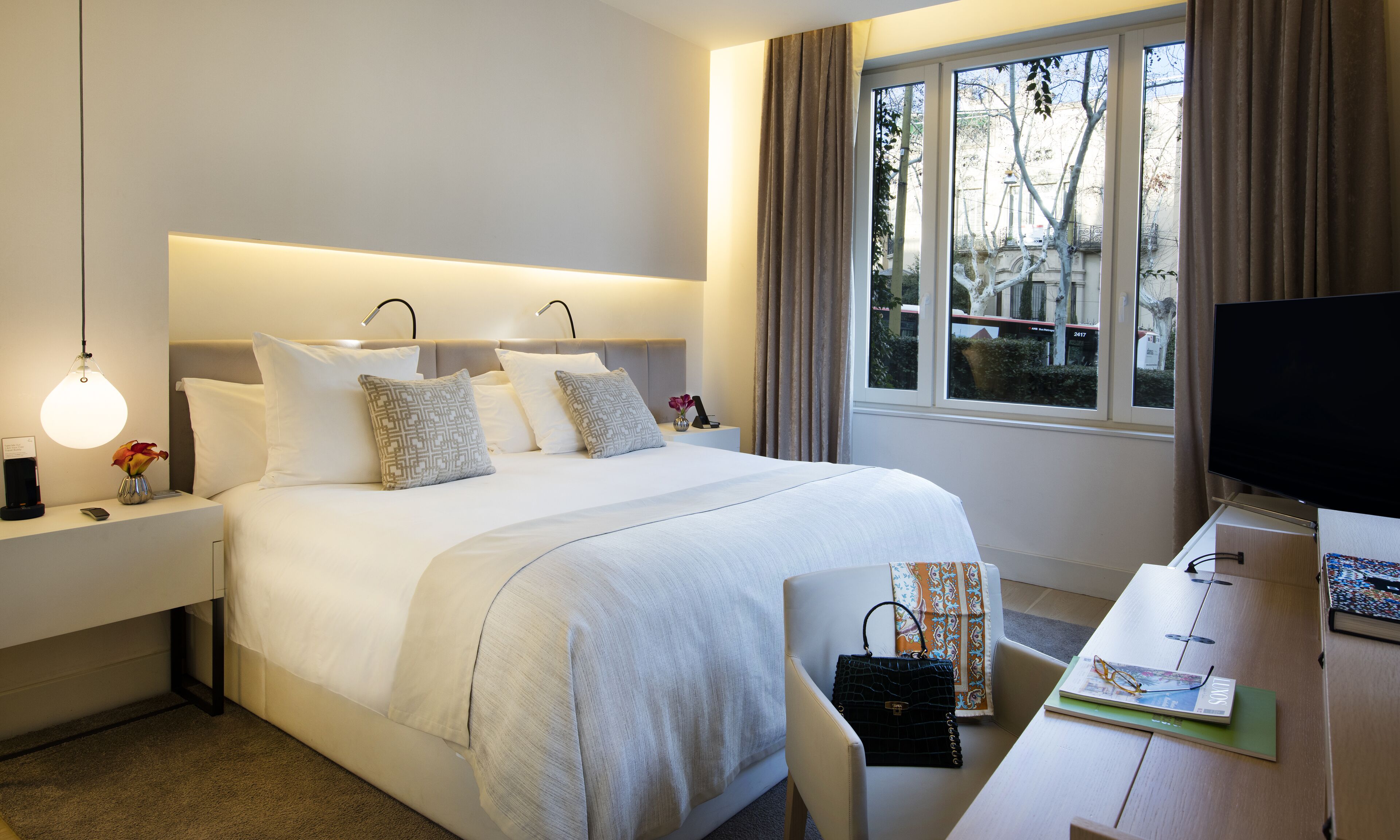 Hotelkamer met een groot bed, nachtkastjes, een bureau met stoel, een televisie en een raam met gordijnen.