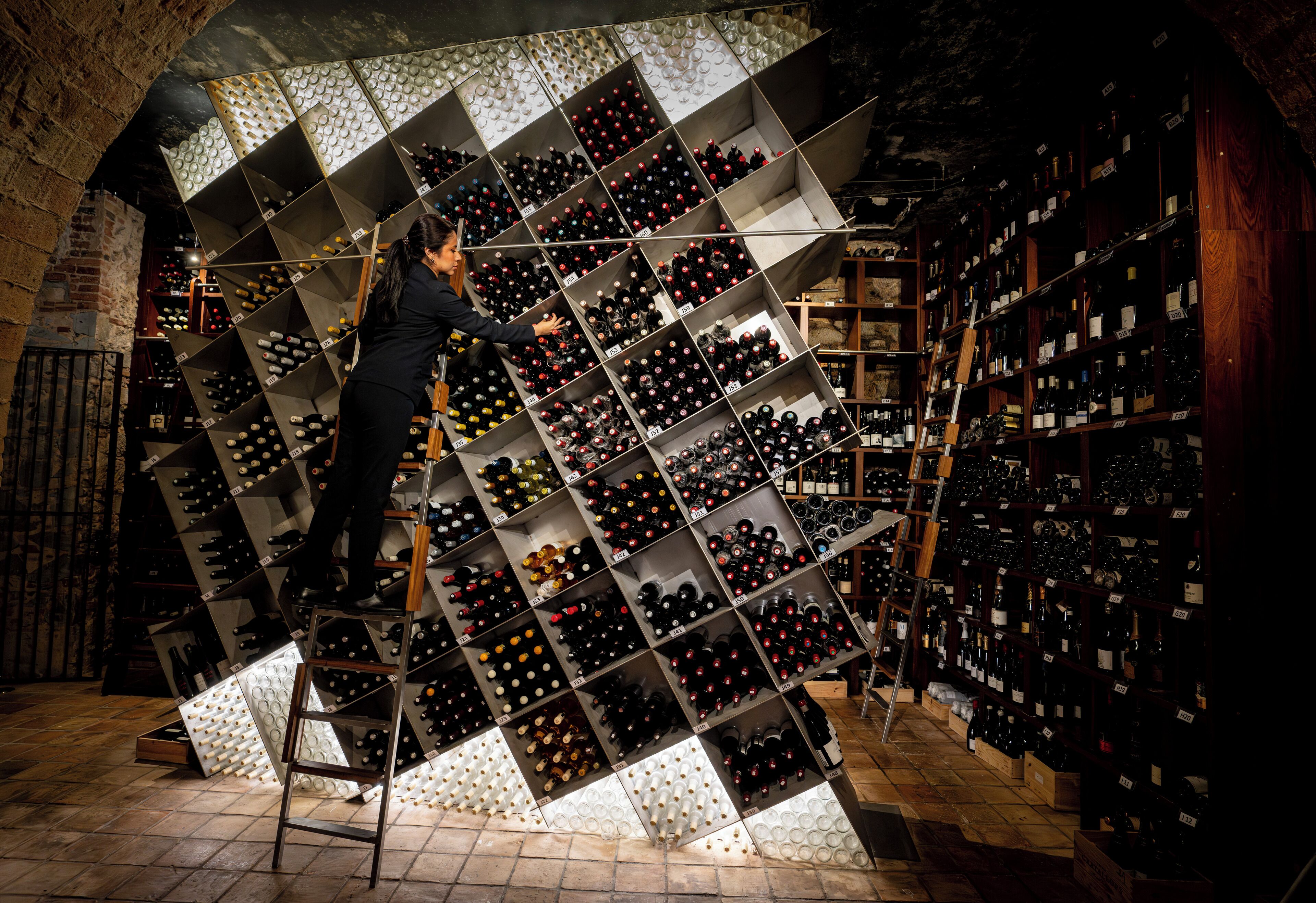 Une cave à vin où une femme range des bouteilles de vin sur une échelle.