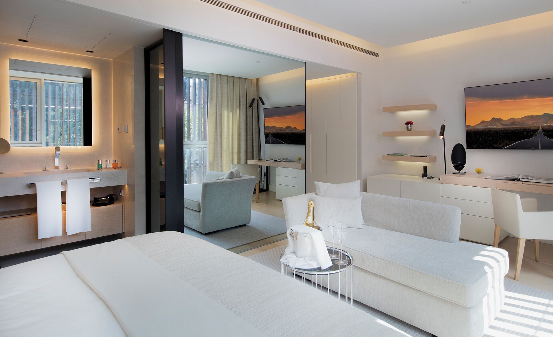 A modern hotel room with a bed, a sofa, a desk, a mirror, and a TV.