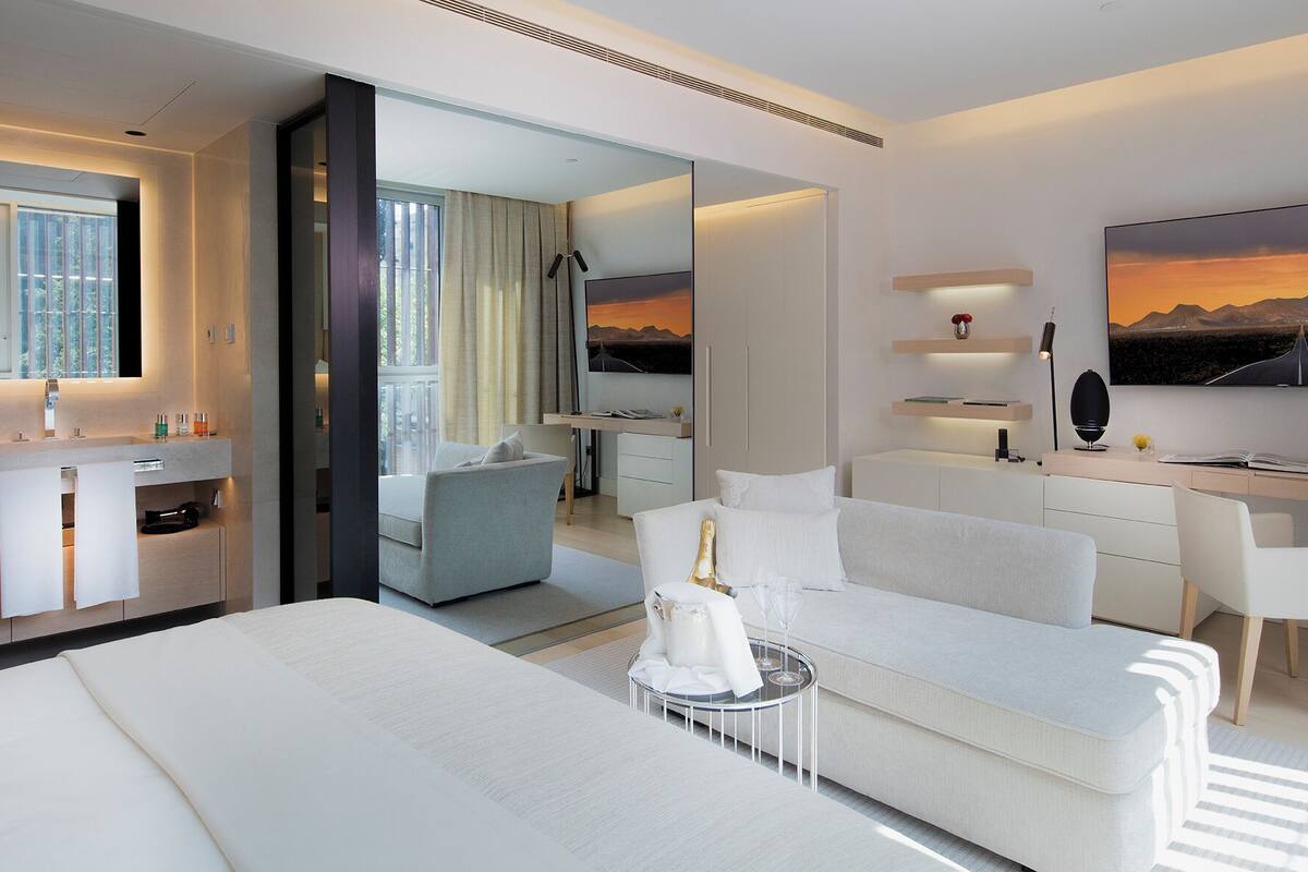 A modern hotel room with a bed, a sofa, a desk, a mirror, and a TV.
