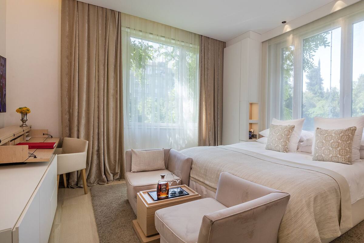 A modern hotel room with a large bed, two bedside tables, a desk, a chair, and a sofa.