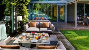 A modern outdoor dining area with a wooden deck, a grey sofa, and a table set with breakfast items. - ABaC Hotel Boutique 5 GL (Barcelona)