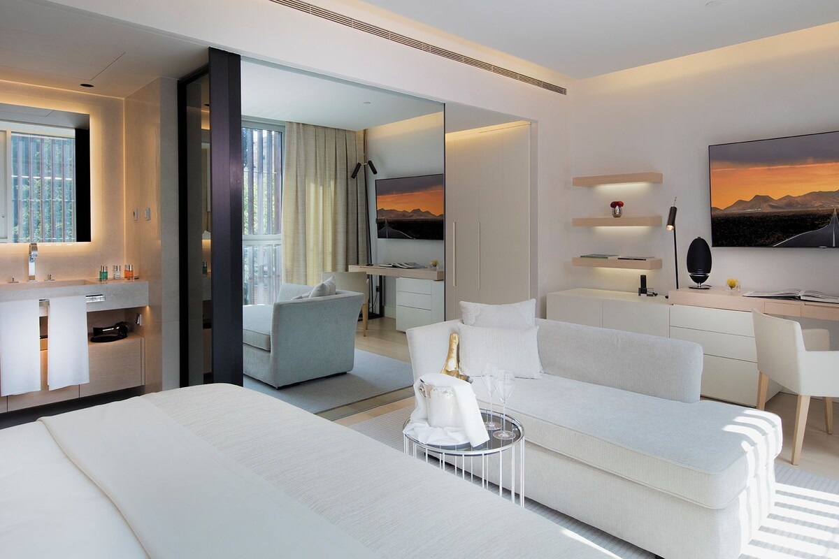 A modern hotel room with a bed, a sofa, a desk, a mirror, and a TV.