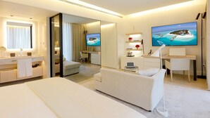 A modern hotel room with a bed, a desk, a chair, a TV, and a large window with a view of a beach. - ABaC Hotel Boutique 5 GL (Barcelona)