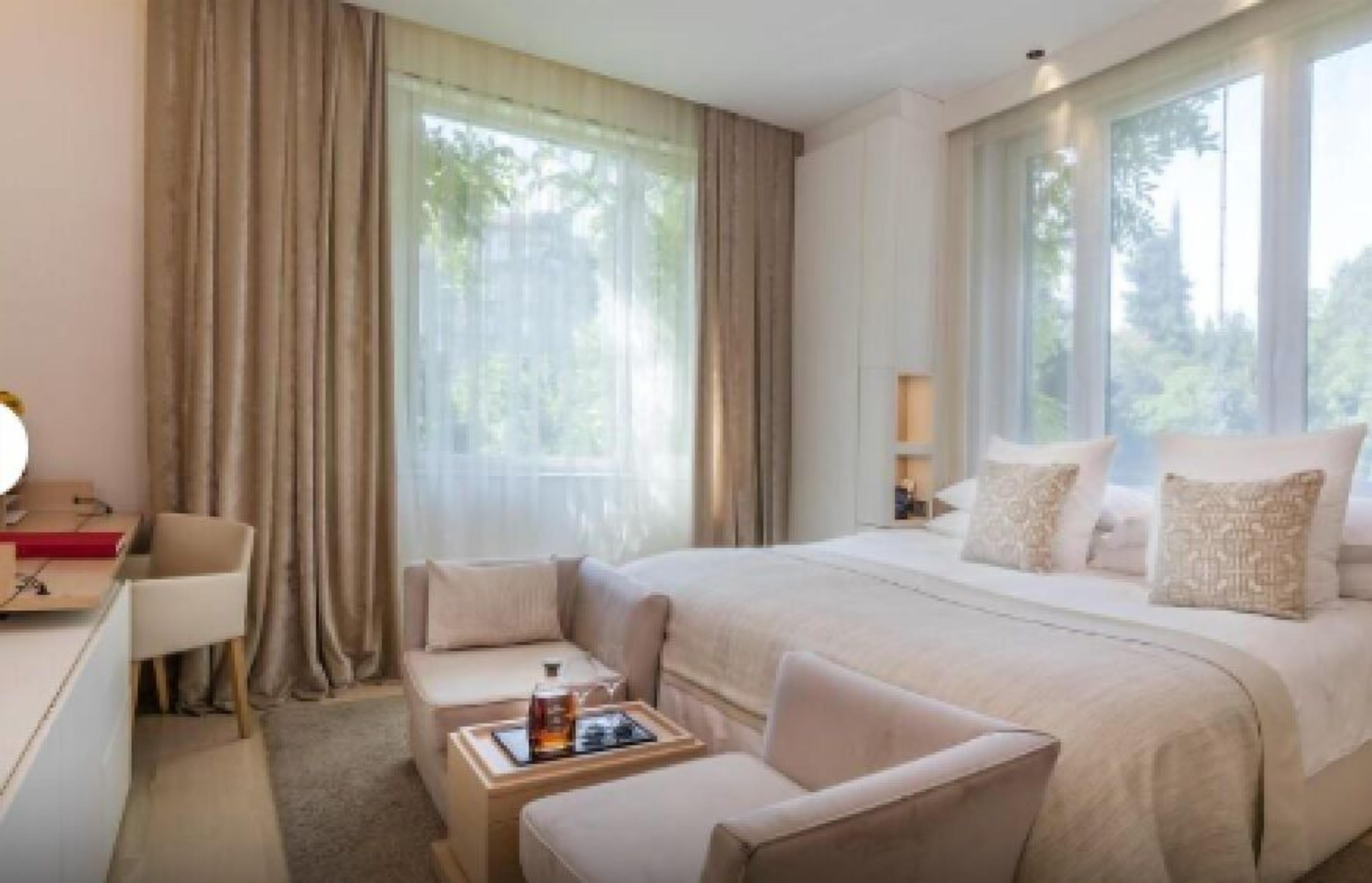 A hotel room with a large bed, a desk, a chair, and a window with curtains.