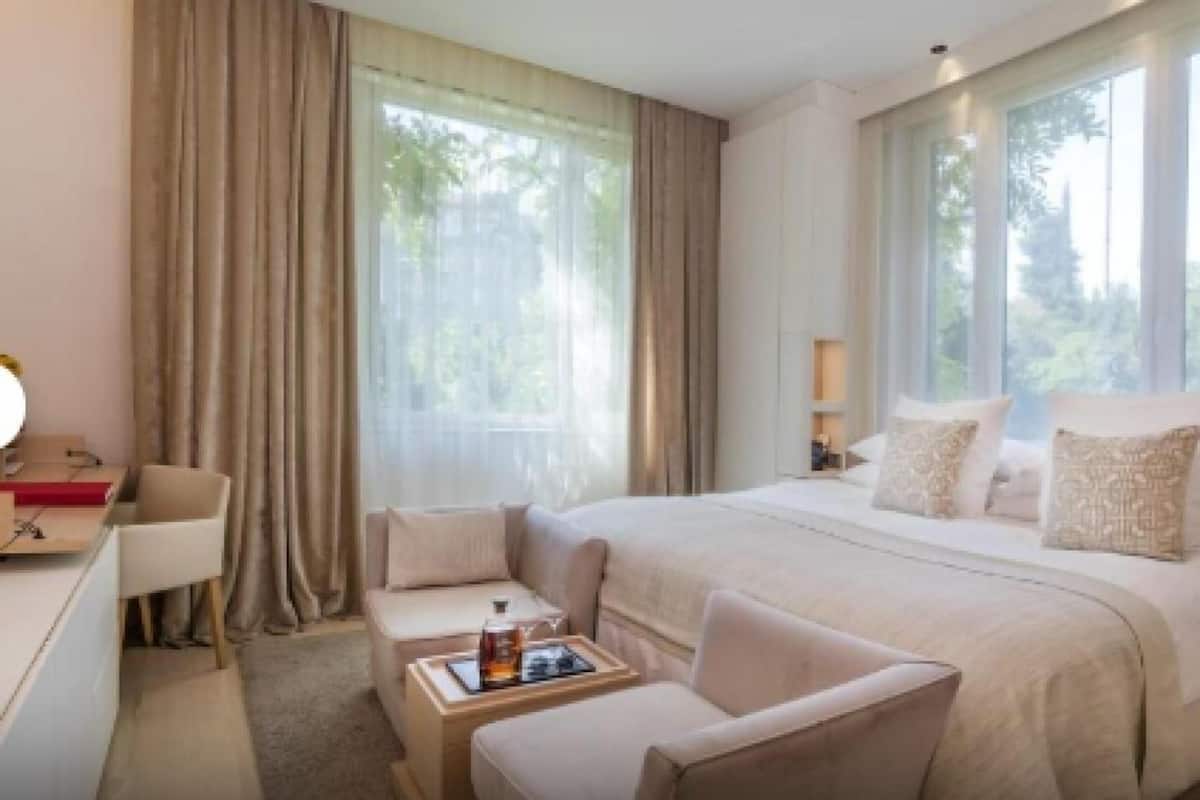 A hotel room with a large bed, a desk, a chair, and a window with curtains.
