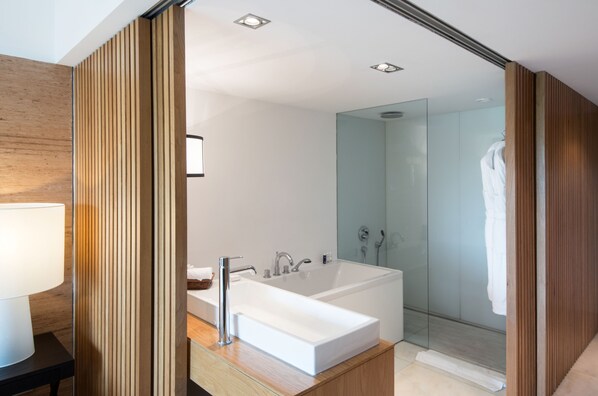Un baño moderno con una bañera blanca grande, ducha con cerramiento de vidrio y paneles de madera.