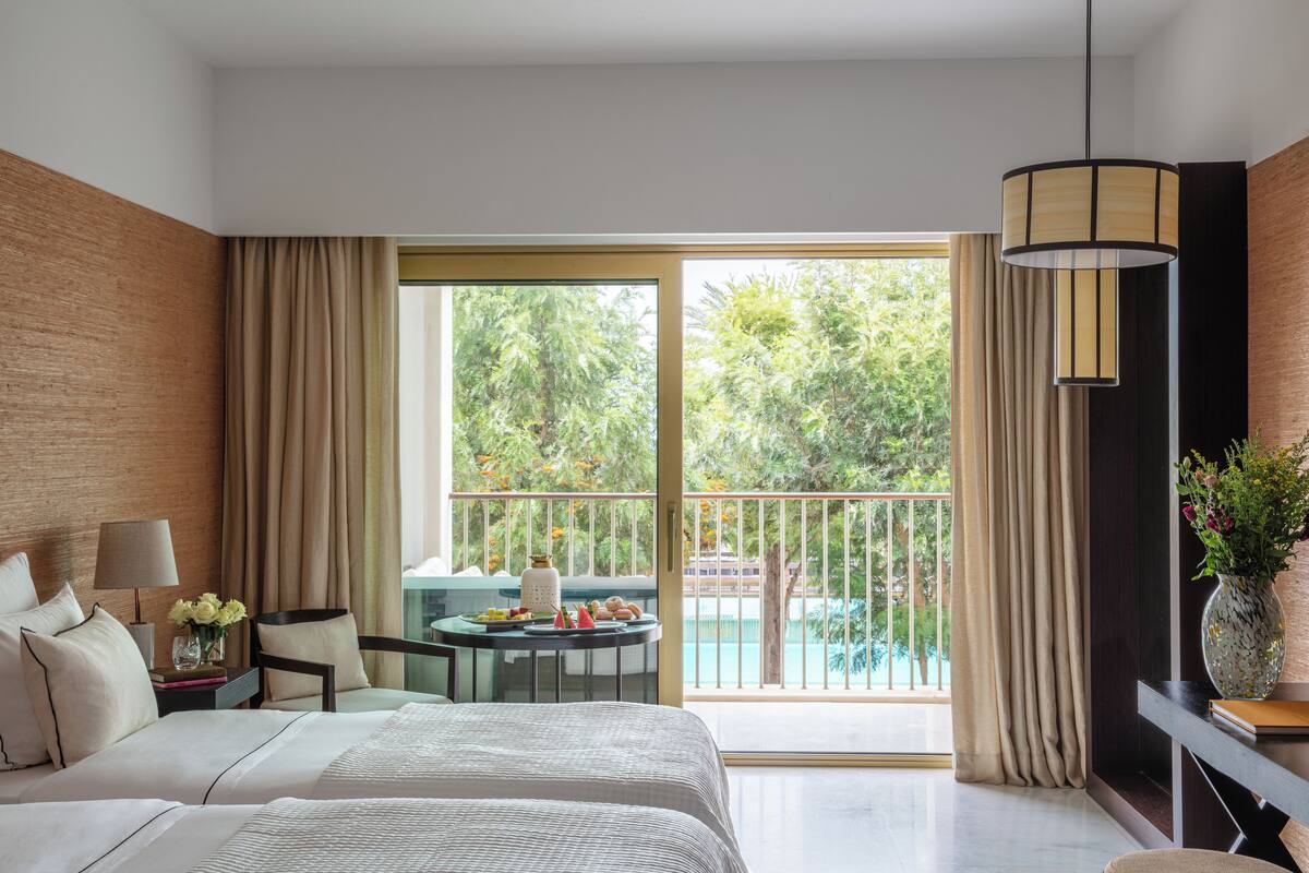 Habitación de hotel con cama, escritorio, silla, una mesa con flores y vistas a una piscina y zonas verdes.