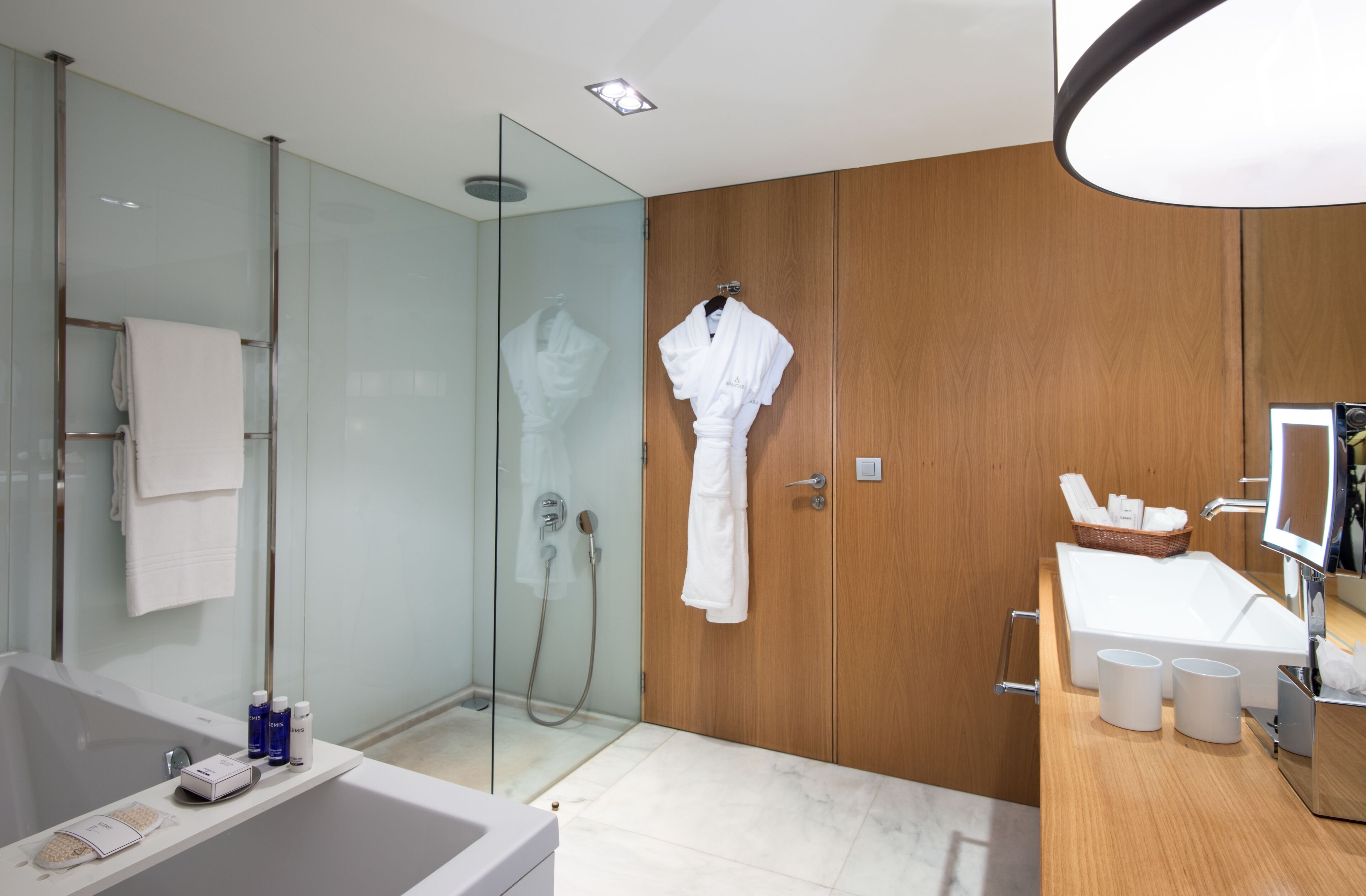 A modern bathroom with a glass shower enclosure, a wooden vanity, and a white bathtub.