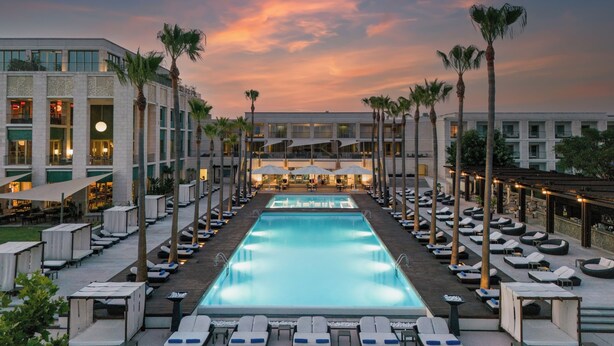 Un hotel con una piscina grande, sillones de descanso y palmeras.