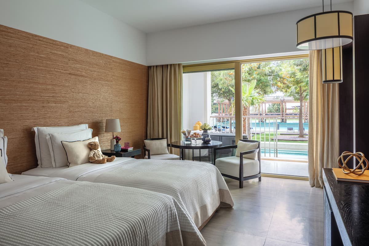 Una habitación de hotel con dos camas, una mesa de comedor y vistas a una piscina.