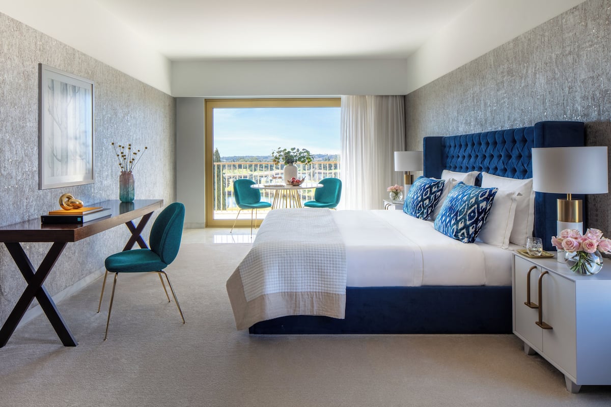 Habitación de hotel con una cama grande, un escritorio, una silla y un balcón con vistas.