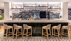 A bar area with a patterned wall, multiple liquor bottles, and bar stools.