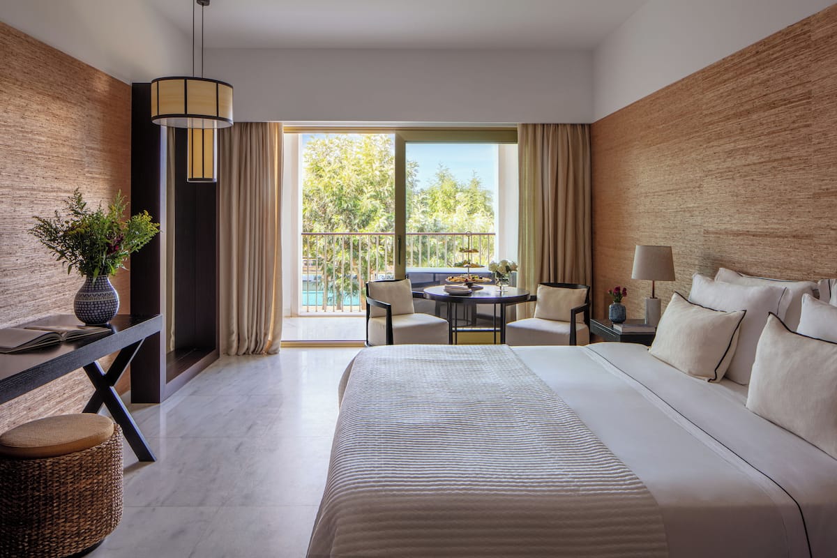 Habitación de hotel moderna con una cama grande, una mesa de comedor y un balcón con vistas a árboles.