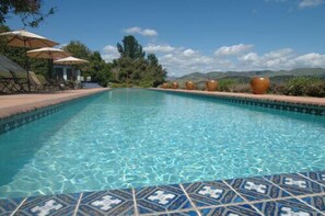 Una piscina cristalina con borde de azulejos, rodeada de mobiliario de exterior y macetas decorativas grandes.