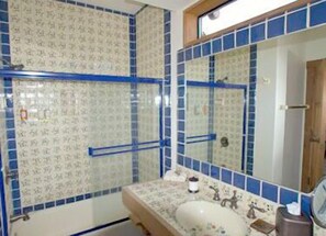 Un baño con lavamanos, espejo y paredes con azulejos azules.