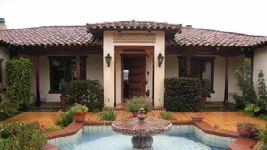 A traditional house with a tiled roof, a central entrance with a decorative arch, and a small fountain in the courtyard.