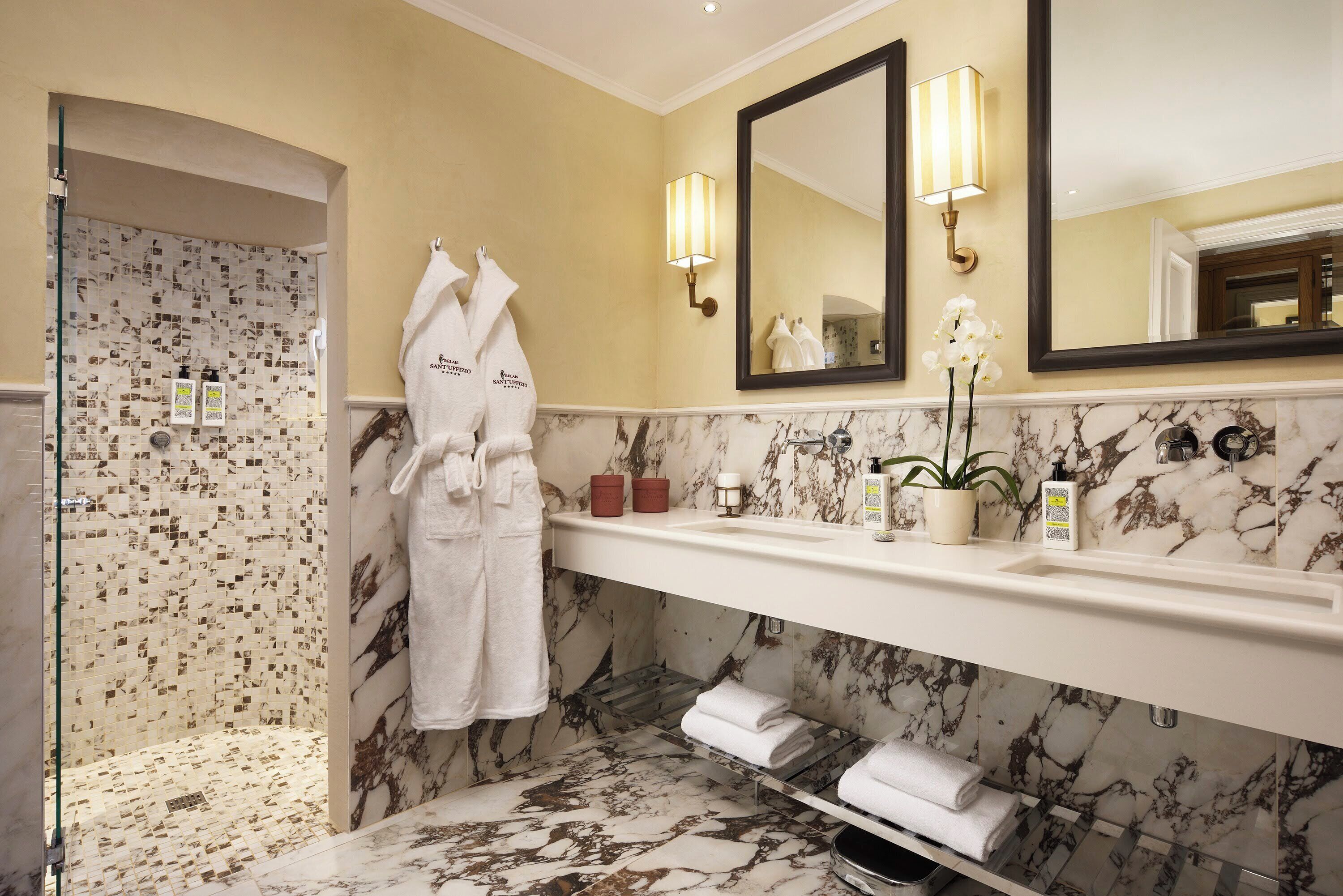 Un bagno con un mobile lavabo in marmo, cabina doccia in vetro e un ampio specchio illuminato da applique.