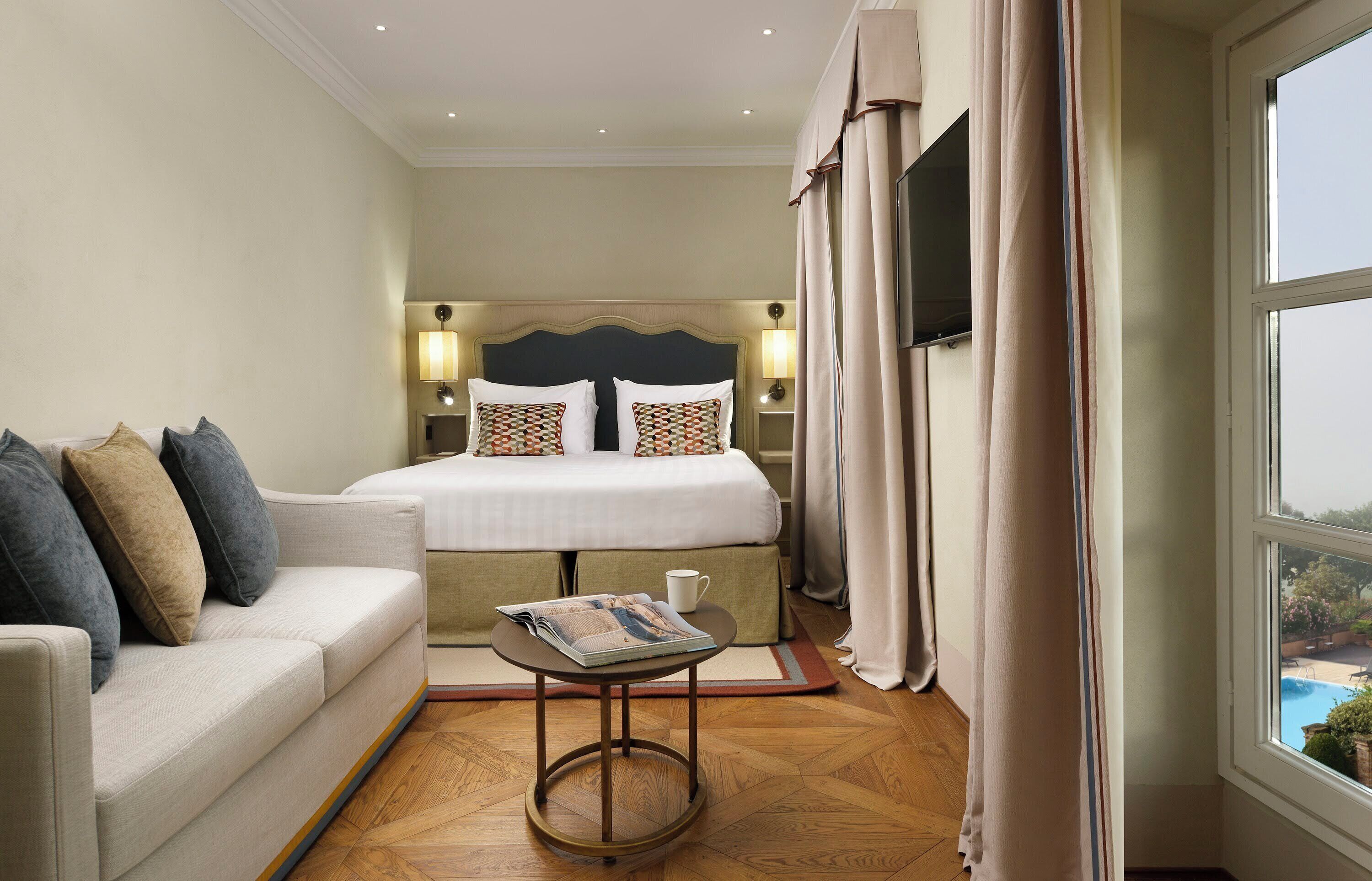 A hotel room with a bed, a sofa, a small table, and a window with curtains.