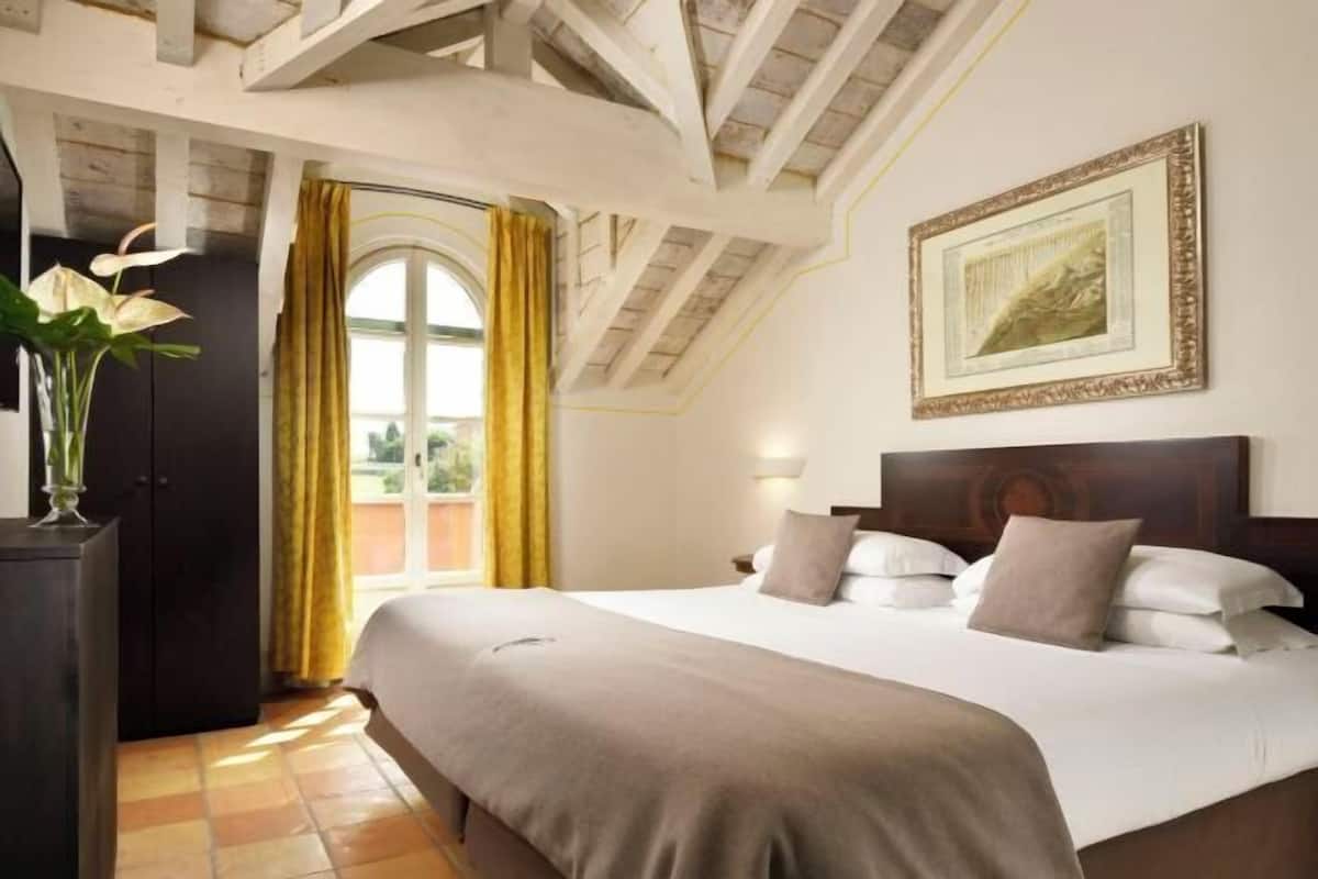 A hotel room with a large bed, a wooden headboard, a framed picture on the wall, and a window with curtains.