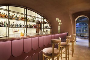 A bar with a curved glass enclosure, multiple shelves of bottles, and bar stools. - Relais Sant'Uffizio (Penango)