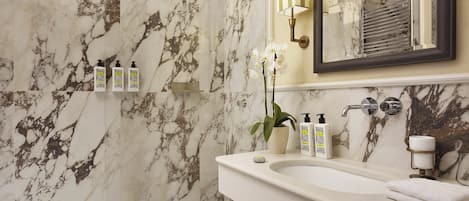 A bathroom with marble walls, a sink, a mirror, and toiletries.