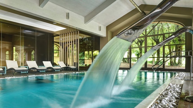 A pool with a water feature, lounge chairs, and a view of greenery.