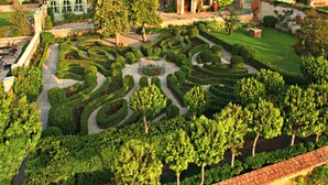 A meticulously landscaped garden with geometric pathways and a central circular area, surrounded by neatly trimmed hedges and trees.