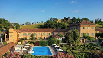 Un edificio grande con piscina, rodeado de jardines cuidados y un paisaje montañoso.