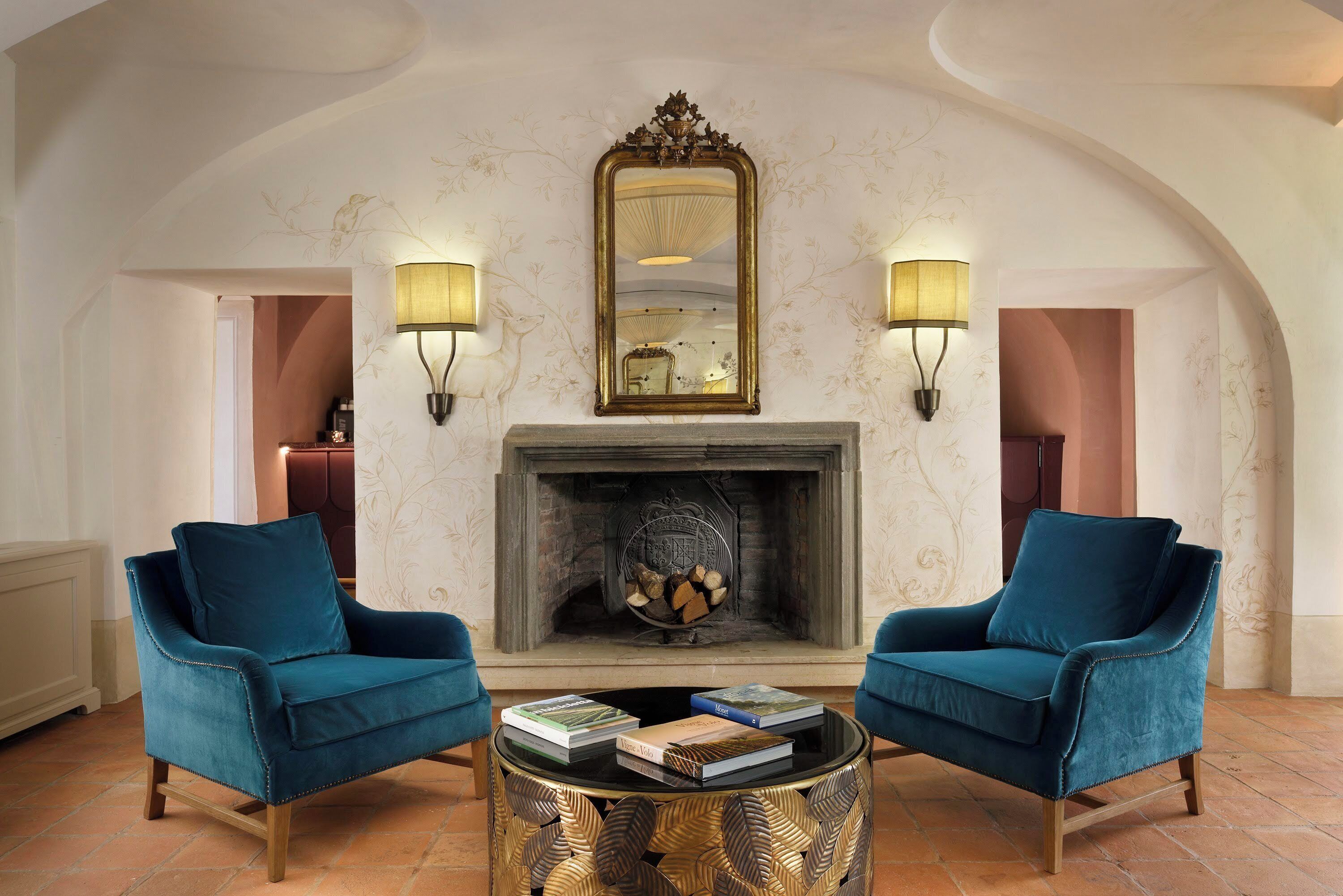 A room with a fireplace, two armchairs, a coffee table with books, and wall-mounted lamps.