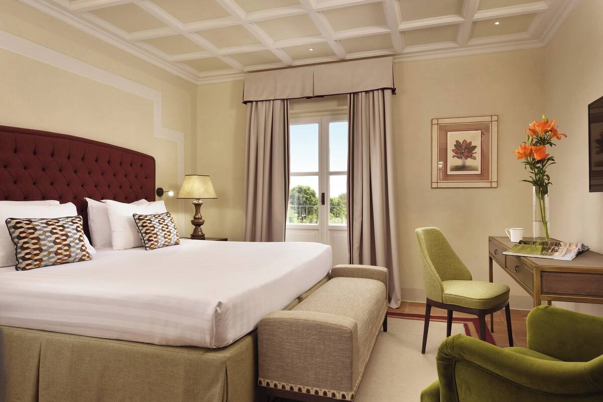 Une chambre d’hôtel avec un grand lit, un bureau, une chaise et une fenêtre avec des rideaux.