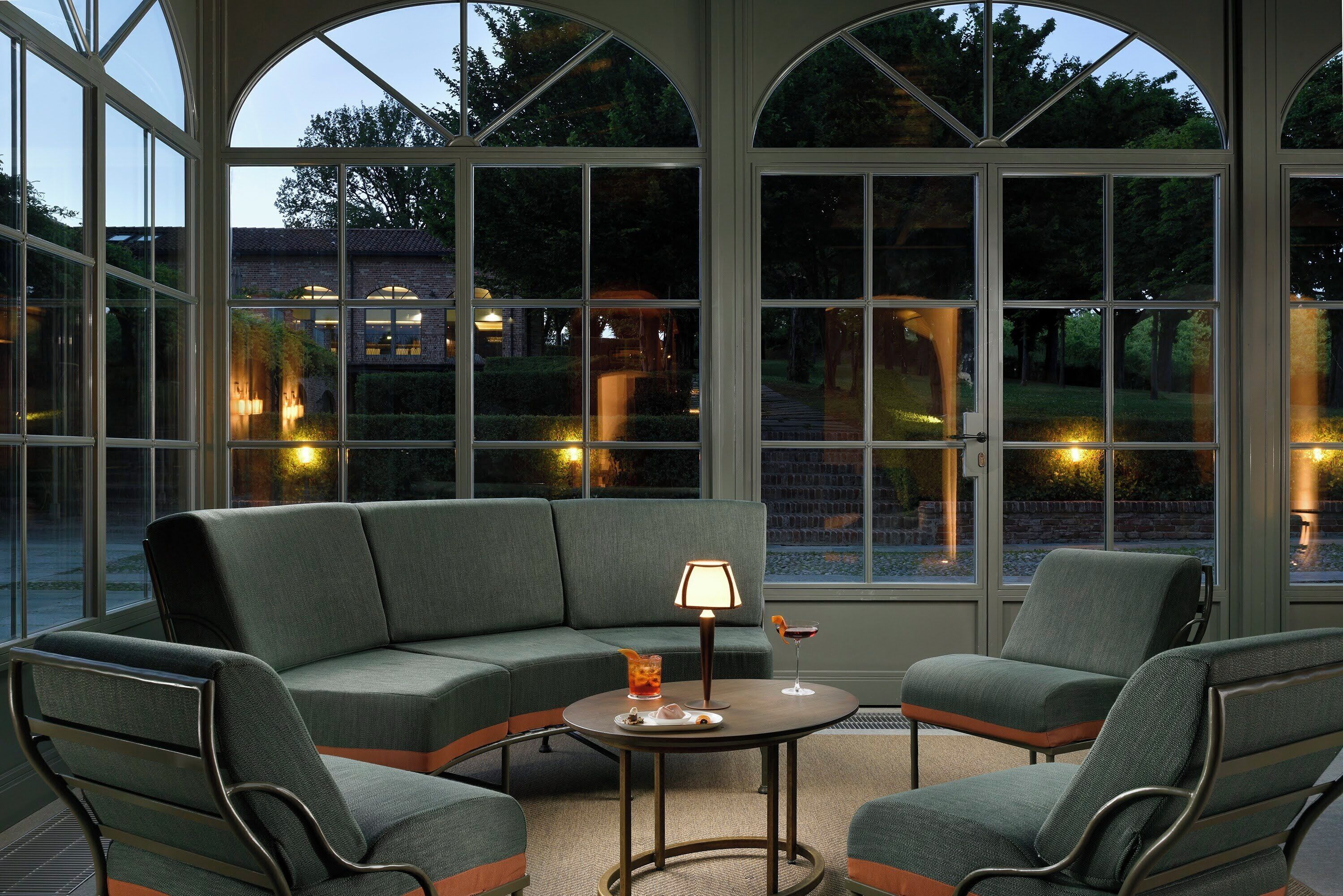 A room with a sectional sofa, two armchairs, a small round table, and a lamp.