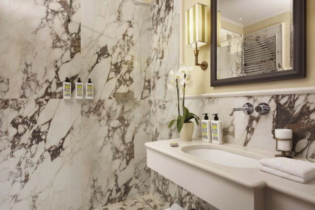 A bathroom with a marble wall, a sink, a mirror, and toiletries.