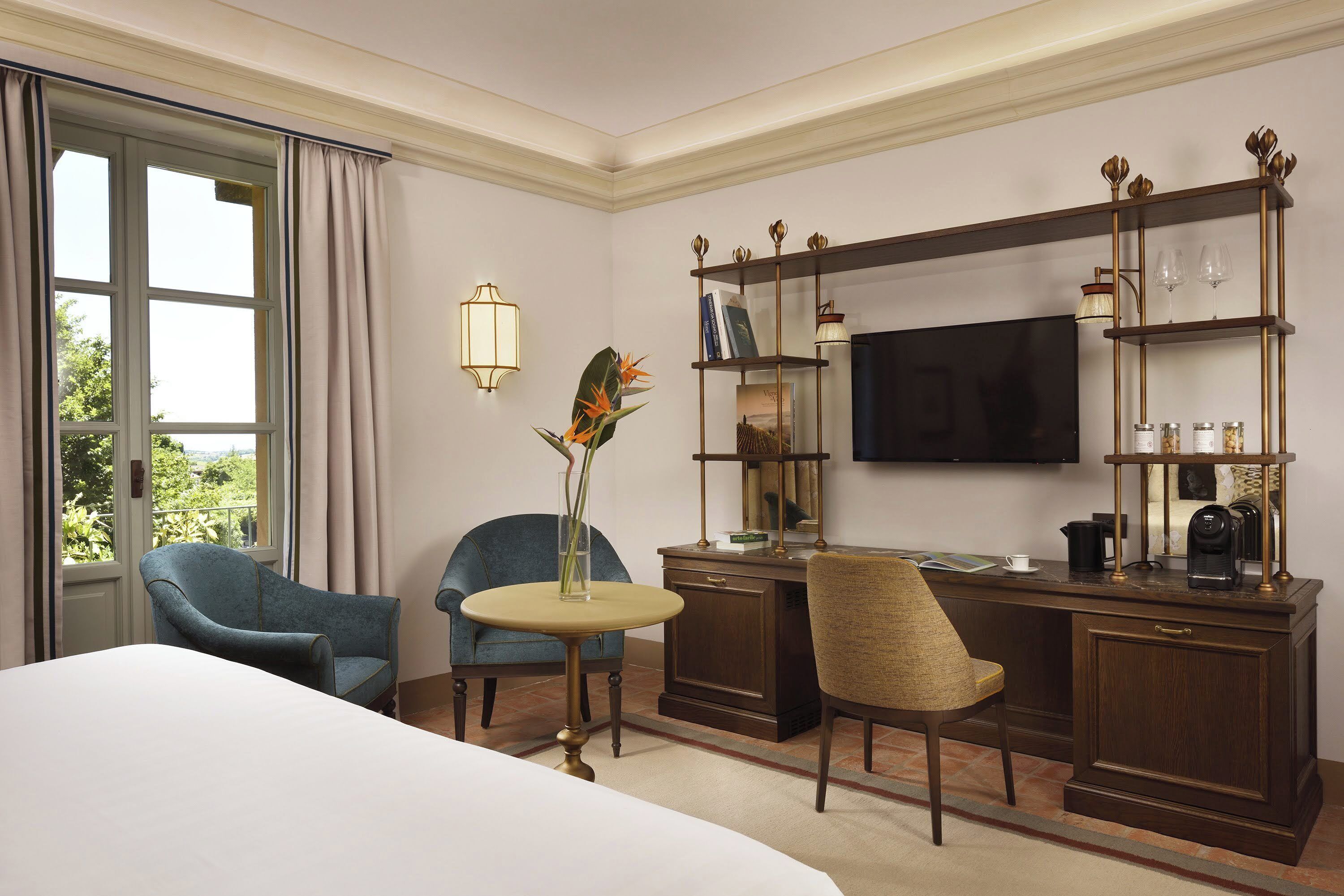 Une chambre d’hôtel comprenant un lit, deux chaises, un bureau avec une télévision, une bibliothèque et une fenêtre avec des rideaux.