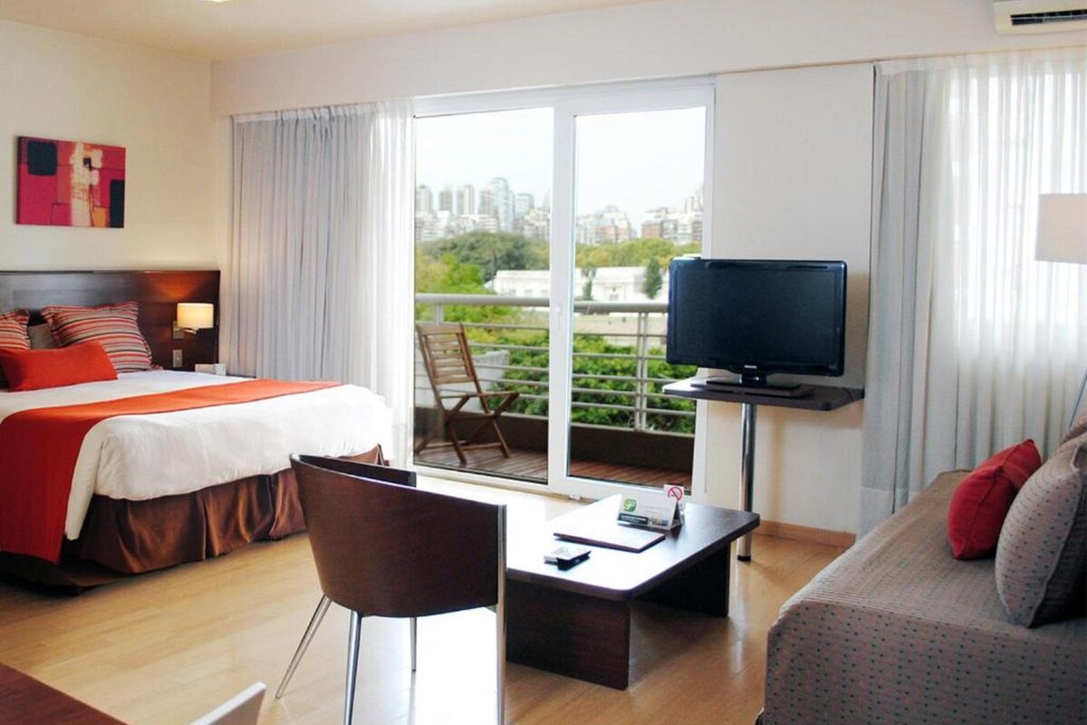 Une chambre d’hôtel comprenant un lit, une télévision, un canapé, un bureau et un balcon avec vue sur la ville.