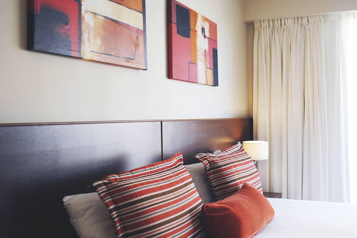 Hotelkamer met een bed, gestreepte kussens, een hoofdbord en abstracte kunst aan de muur.
