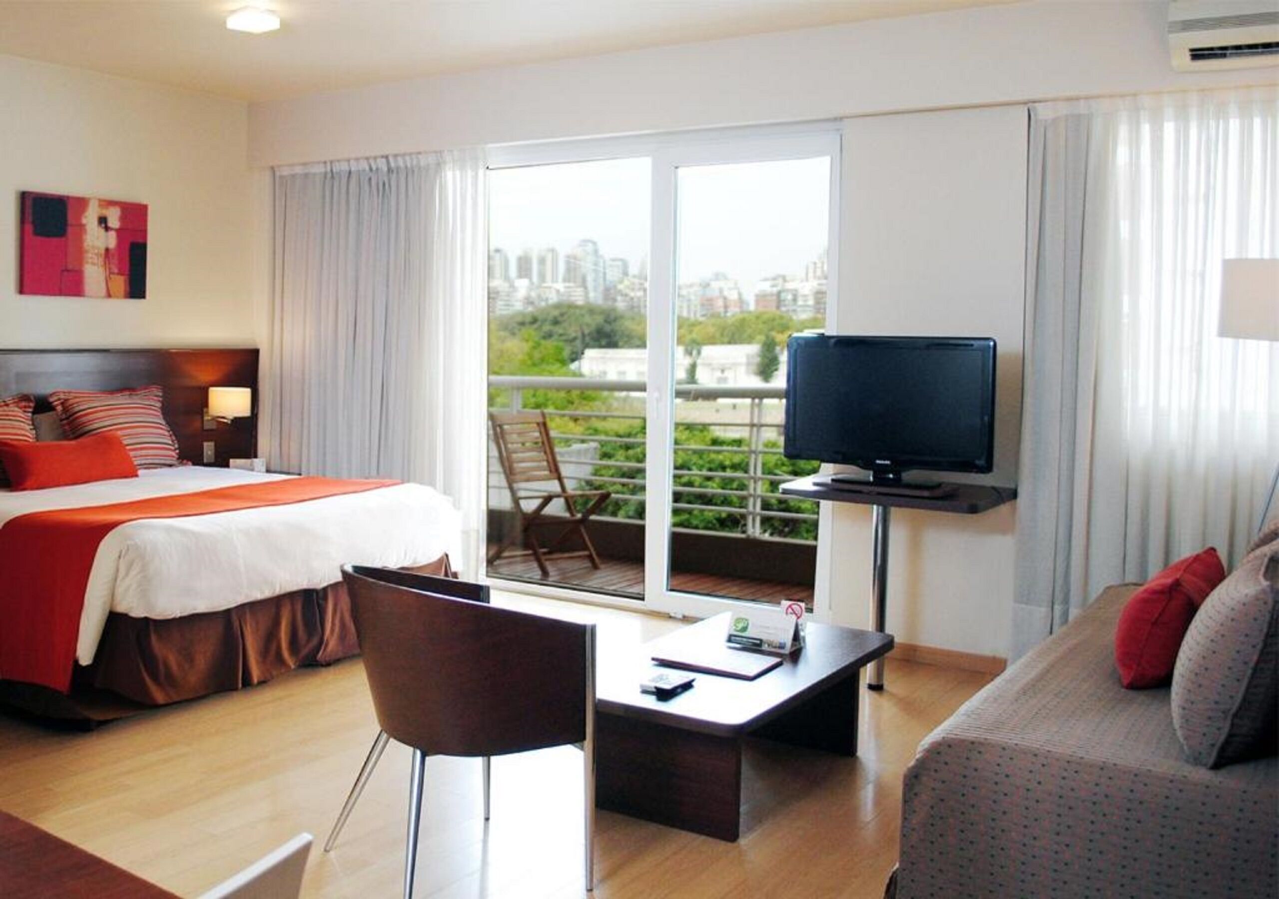Une chambre d’hôtel comprenant un lit, une télévision, un canapé, un bureau et un balcon avec vue sur la ville.