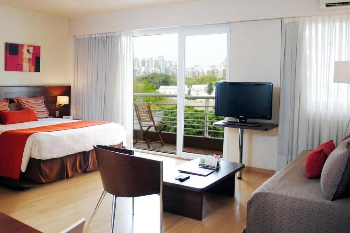 Hotelkamer met een bed, televisie, bank, bureau en balkon met uitzicht over de stad.