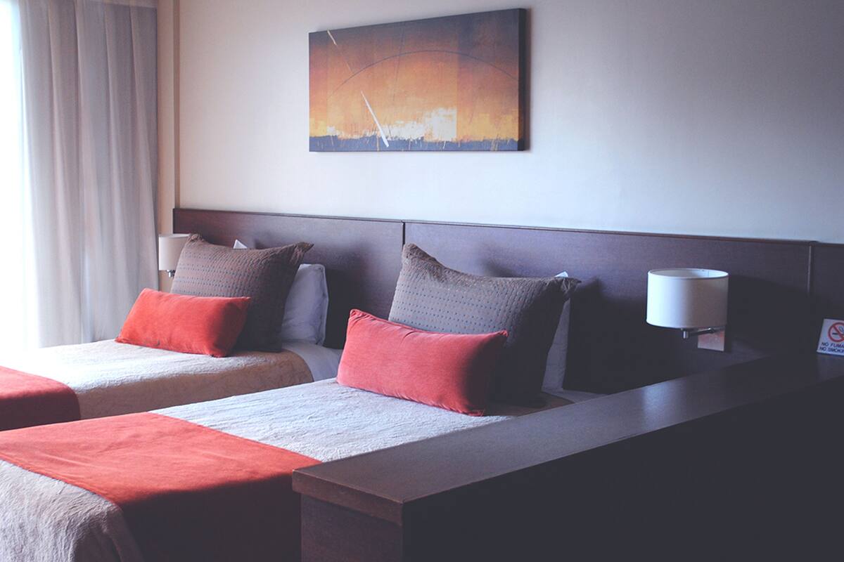 Een hotelkamer met twee bedden, een nachtkastje, een lamp en een schilderij aan de muur.