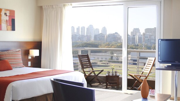 Hotelkamer met een bed, een bureau, een stoel, een televisie en een balkon met uitzicht over de stad.