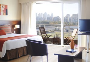 Habitació d'hotel amb llit, escriptori, cadira, televisió i un balcó amb vista a la ciutat.