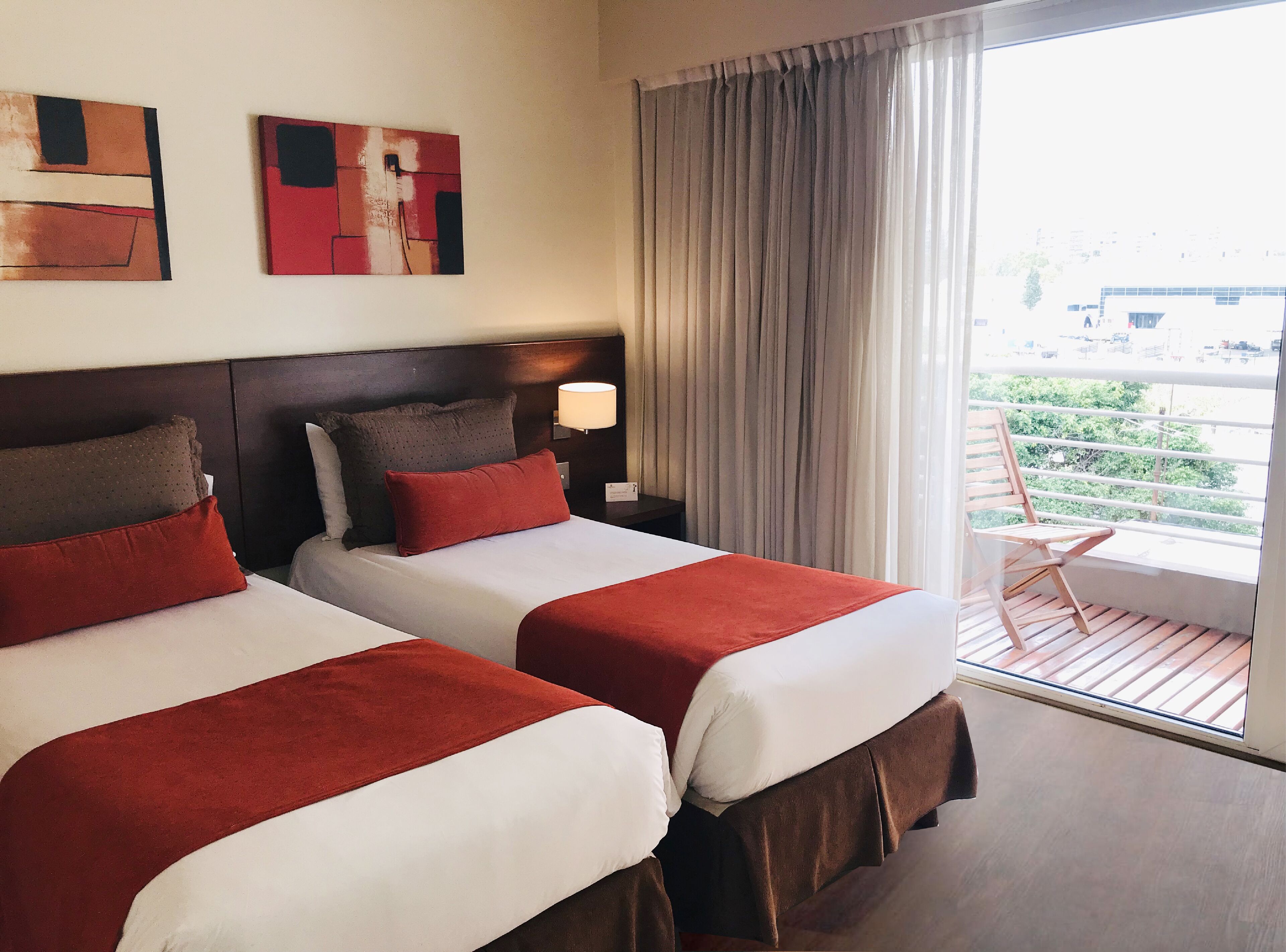 A hotel room with two beds, a large window with curtains, and artwork on the wall.