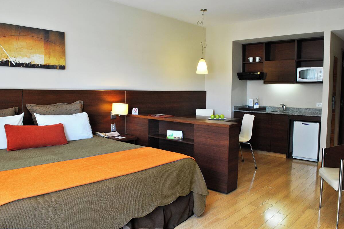 Une chambre d’hôtel avec un lit, un bureau, une kitchenette et un tableau au mur.