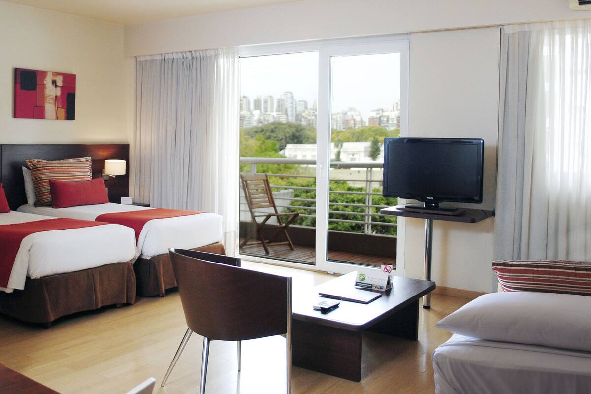 Een hotelkamer met twee bedden, een televisie, een bureau en een balkon met uitzicht op de stad.