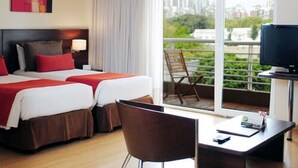 Hotelkamer met twee bedden, een bureau, een stoel, een televisie en een balkon met uitzicht over de stad.