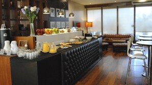 Een moderne hotellobby met een zwarte receptiebalie, een zithoek met een bruine bank en een eetgedeelte met een ronde tafel en barkrukken.