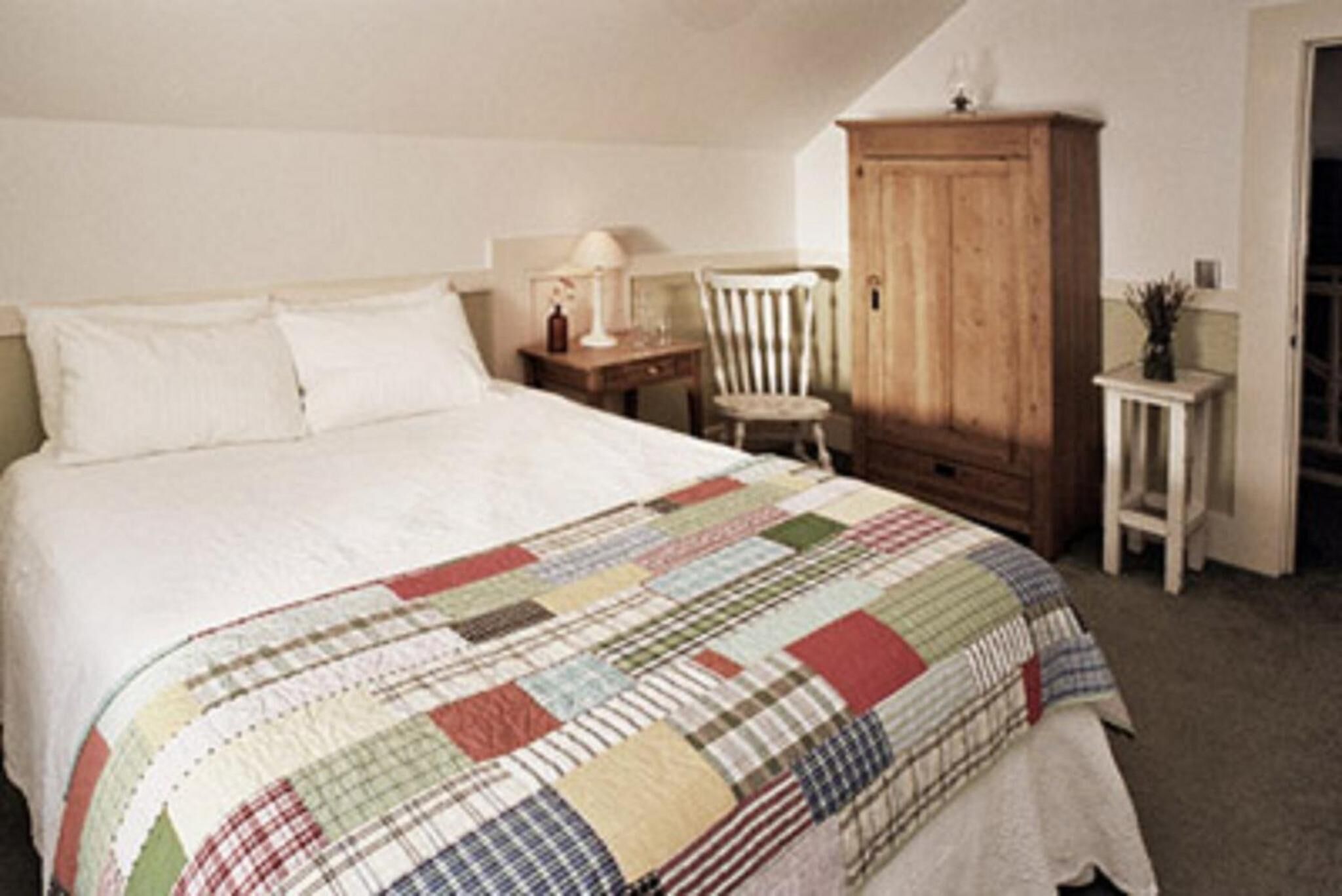 Une chambre à coucher avec un lit, une armoire en bois, une chaise et une petite table avec une lampe.